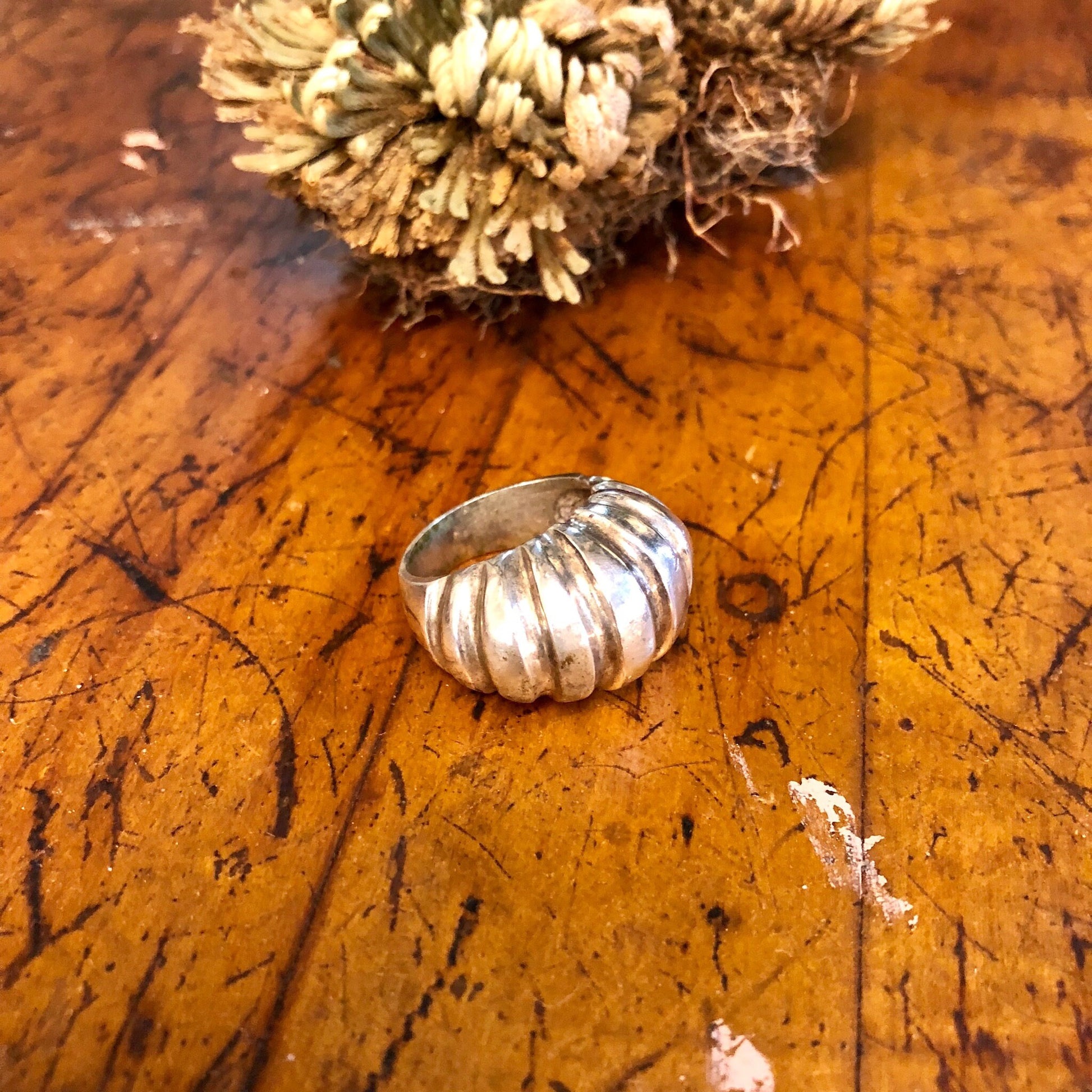 Vintage sterling silver statement ring with ridged design on weathered wooden surface next to dried flowers