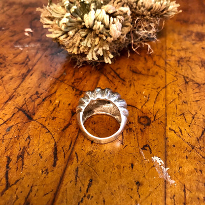 Vintage sterling silver statement ring with ridged design on weathered wooden surface next to dried flowers