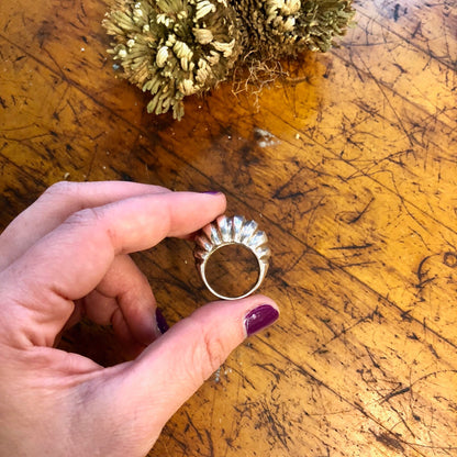 Vintage sterling silver ridged statement ring held in hand above wooden surface with gold decorative flowers.