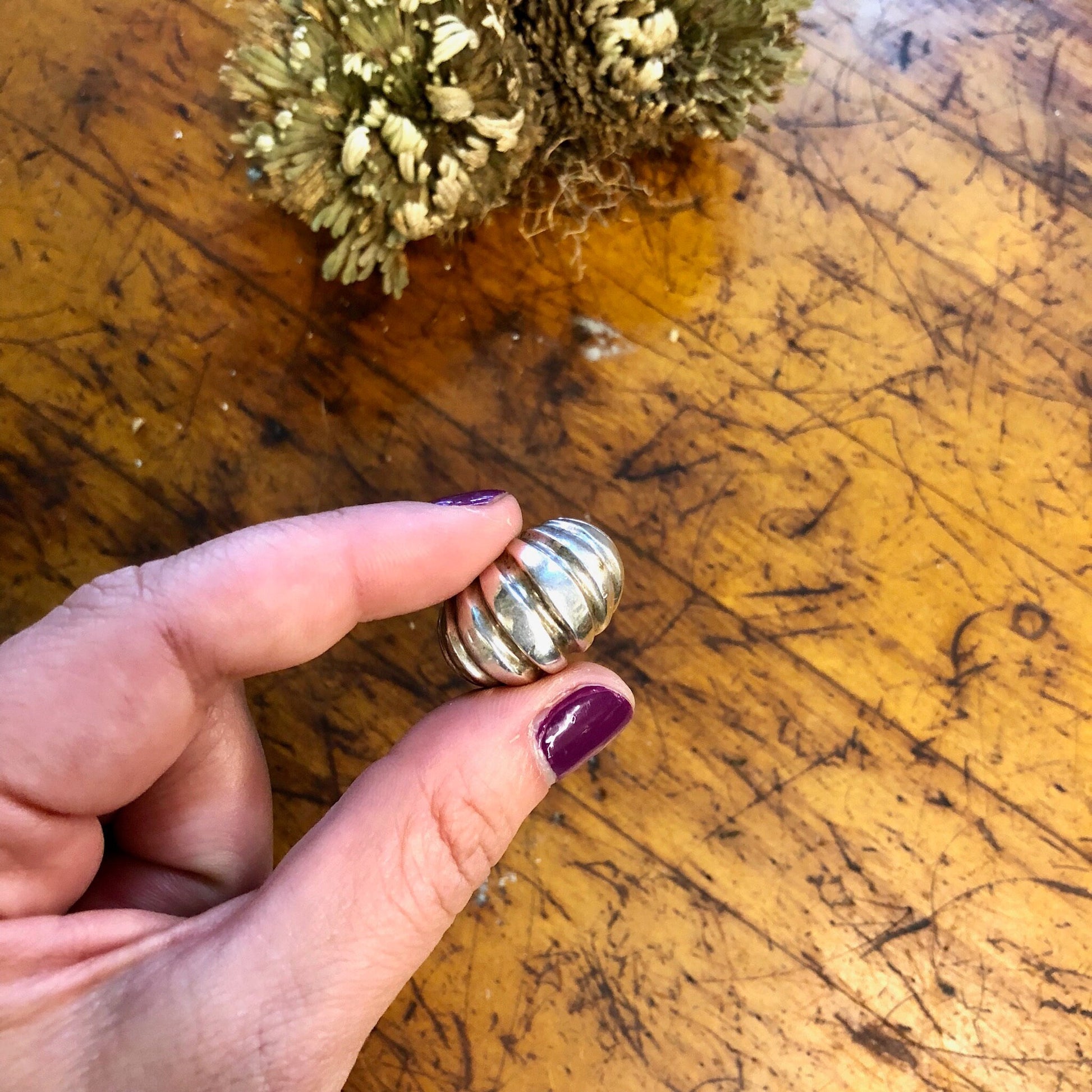 Vintage sterling silver statement ring with ridged design held in front of dried flowers on a wooden surface