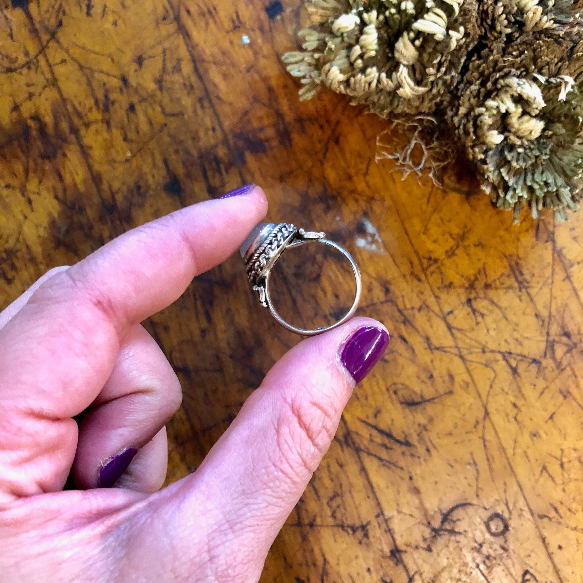 Vintage sterling silver ring with iridescent moonstone displayed on woman's hand against aged wooden surface with pine cones