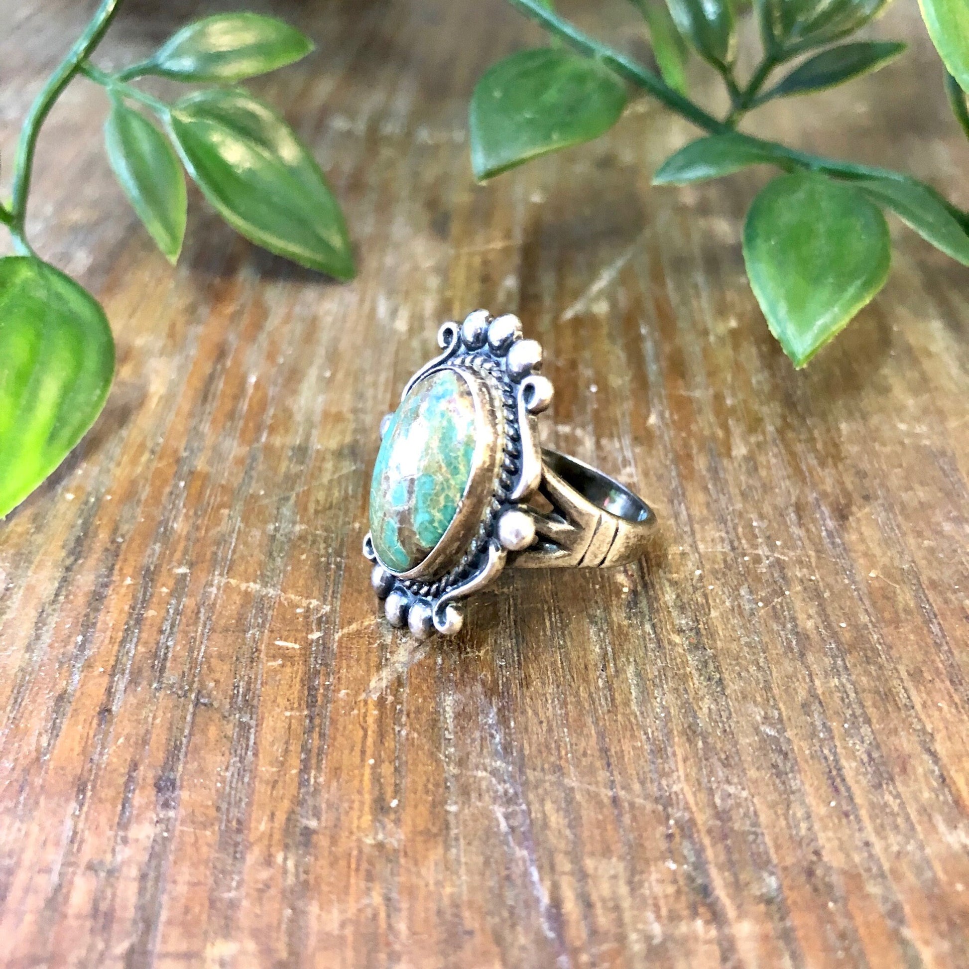 Vintage sterling silver ring with blue Royston turquoise cabochon, set against a wooden surface with green foliage in the background, showcasing bohemian jewelry style.