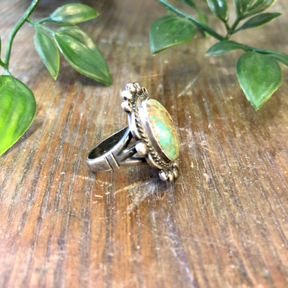 Vintage sterling silver ring featuring a blue Royston turquoise cabochon, set against green leaves on a rustic wooden surface, creating a bohemian jewelry aesthetic.