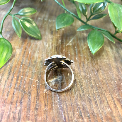 Vintage sterling silver ring featuring a blue Royston turquoise cabochon surrounded by leaf branches on a rustic wooden surface.