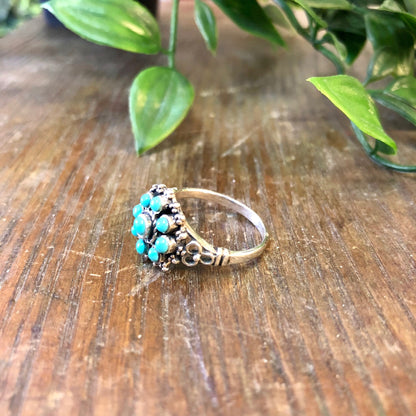 Vintage sterling silver ring with turquoise beads on wooden surface surrounded by green leaves