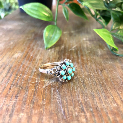 Vintage sterling silver ring with turquoise beads on a wooden surface surrounded by green leaves