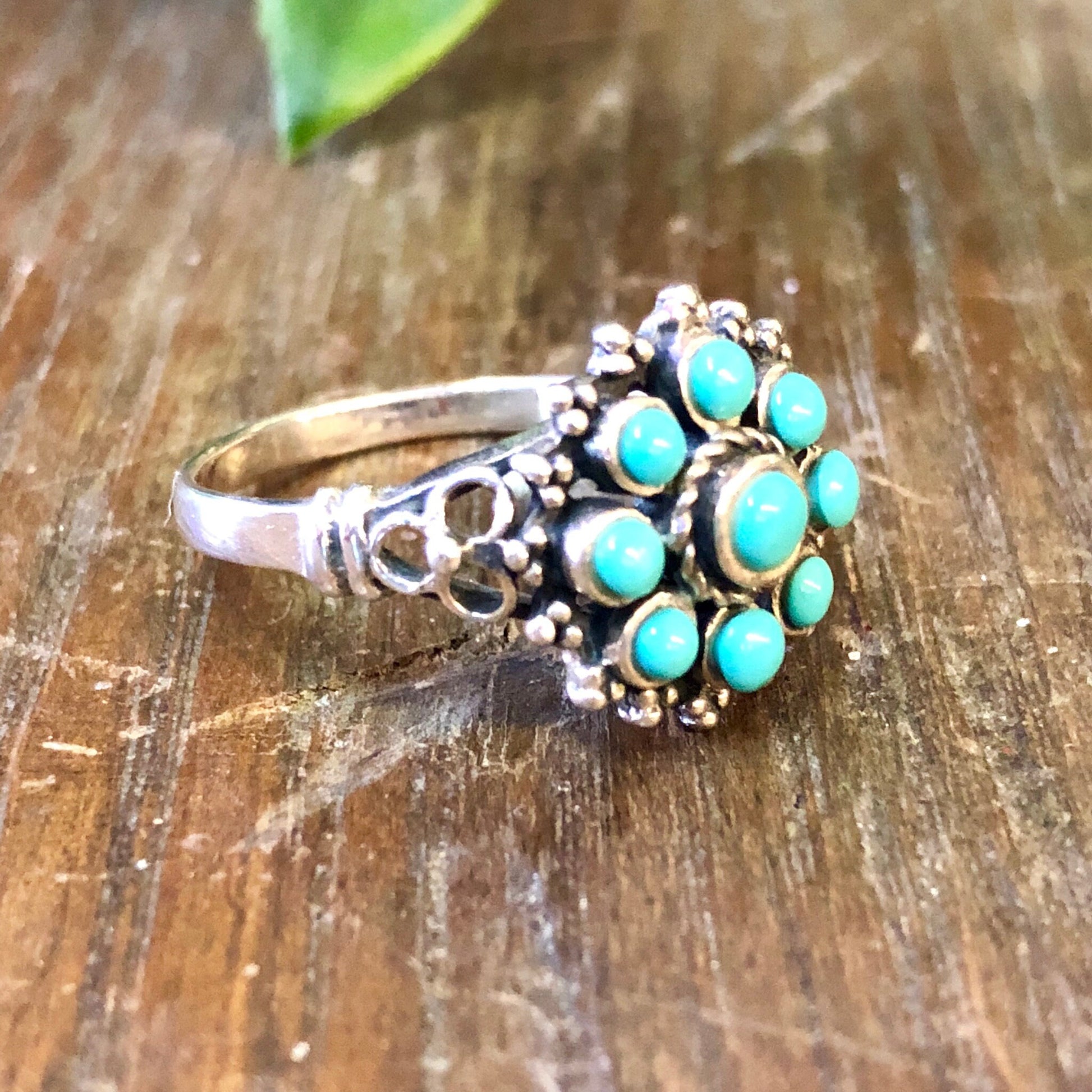 Vintage sterling silver ring with turquoise beads in a bohemian style, placed on a wooden surface.