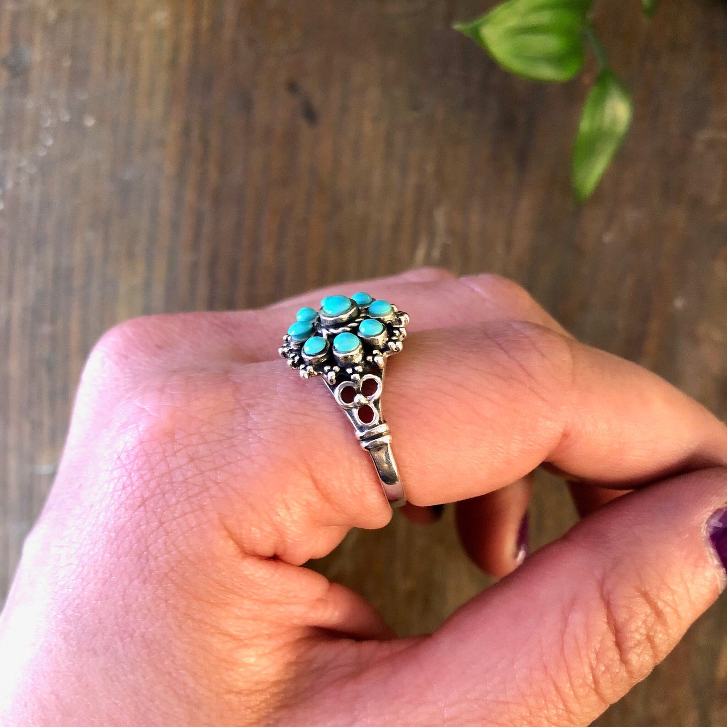 Vintage sterling silver ring with turquoise beads on a person's hand against a wooden background