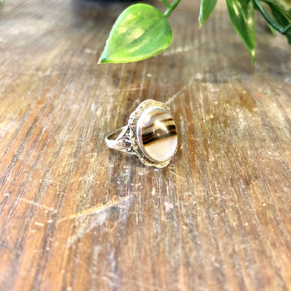 Alt text: Vintage sterling silver ring with brown striped agate gemstone on wooden surface with green leaves, bohemian jewelry, US size 5.5.