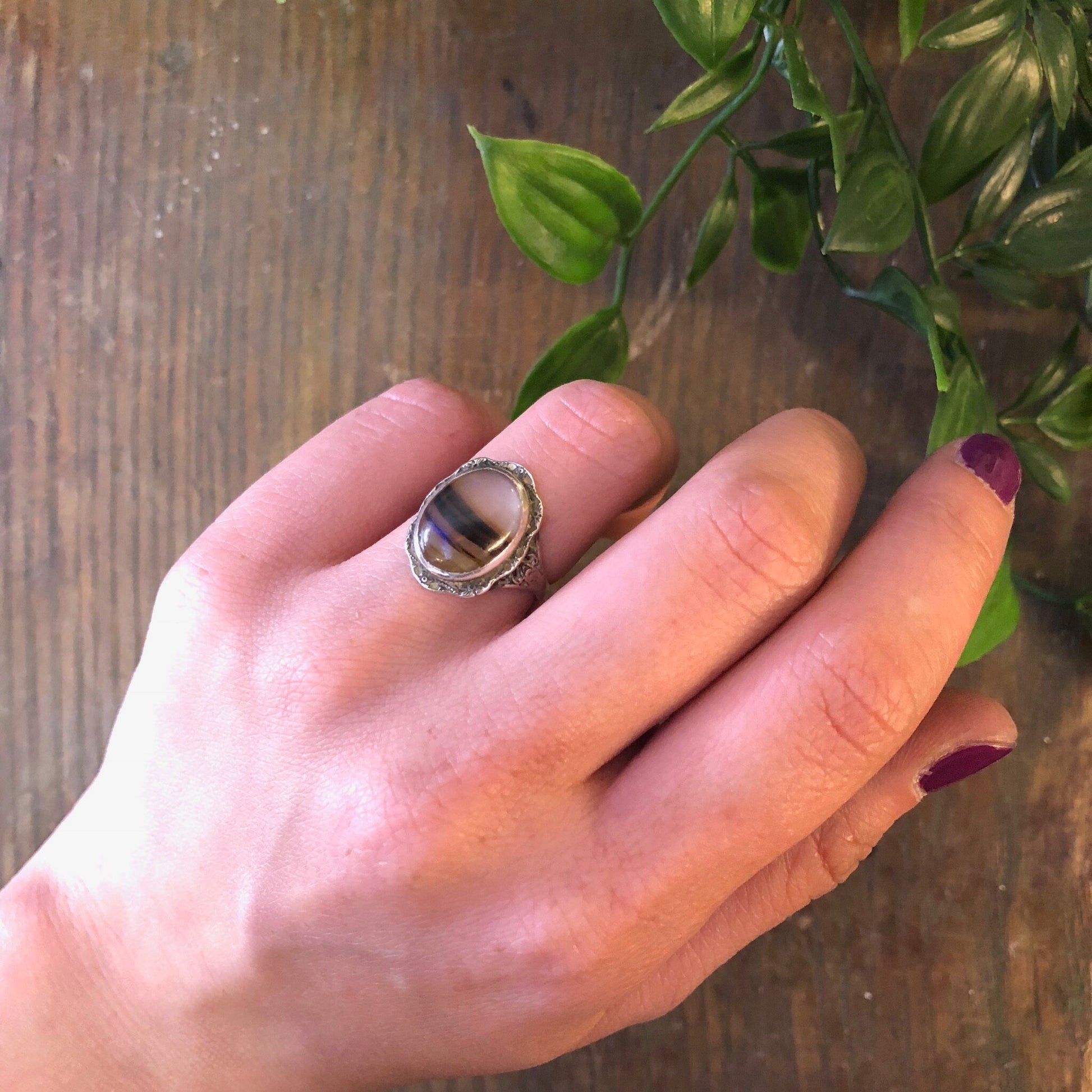 Vintage sterling silver ring with striped brown agate stone on hand next to green plant leaves