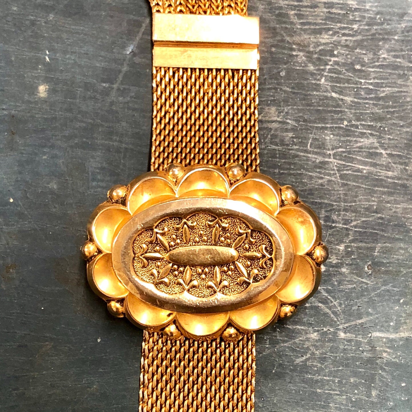 Vintage gold-toned link bracelet with ornate floral design and tassel detail on textured metal background