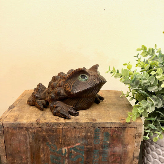 Vintage hand carved wooden frog figurine on rustic wood surface with green plant