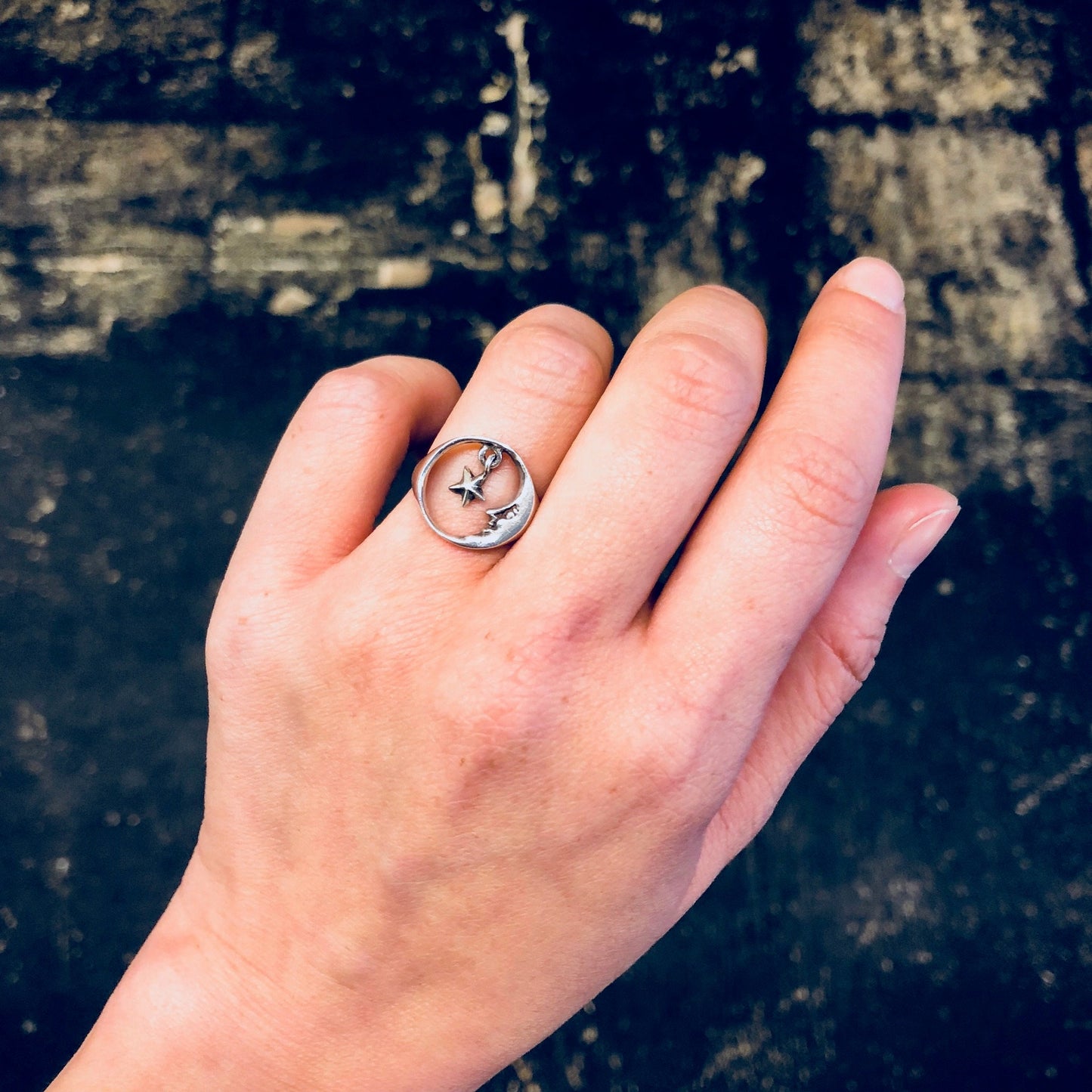 Vintage silver moon and star cut-out ring on hand against textured dark background