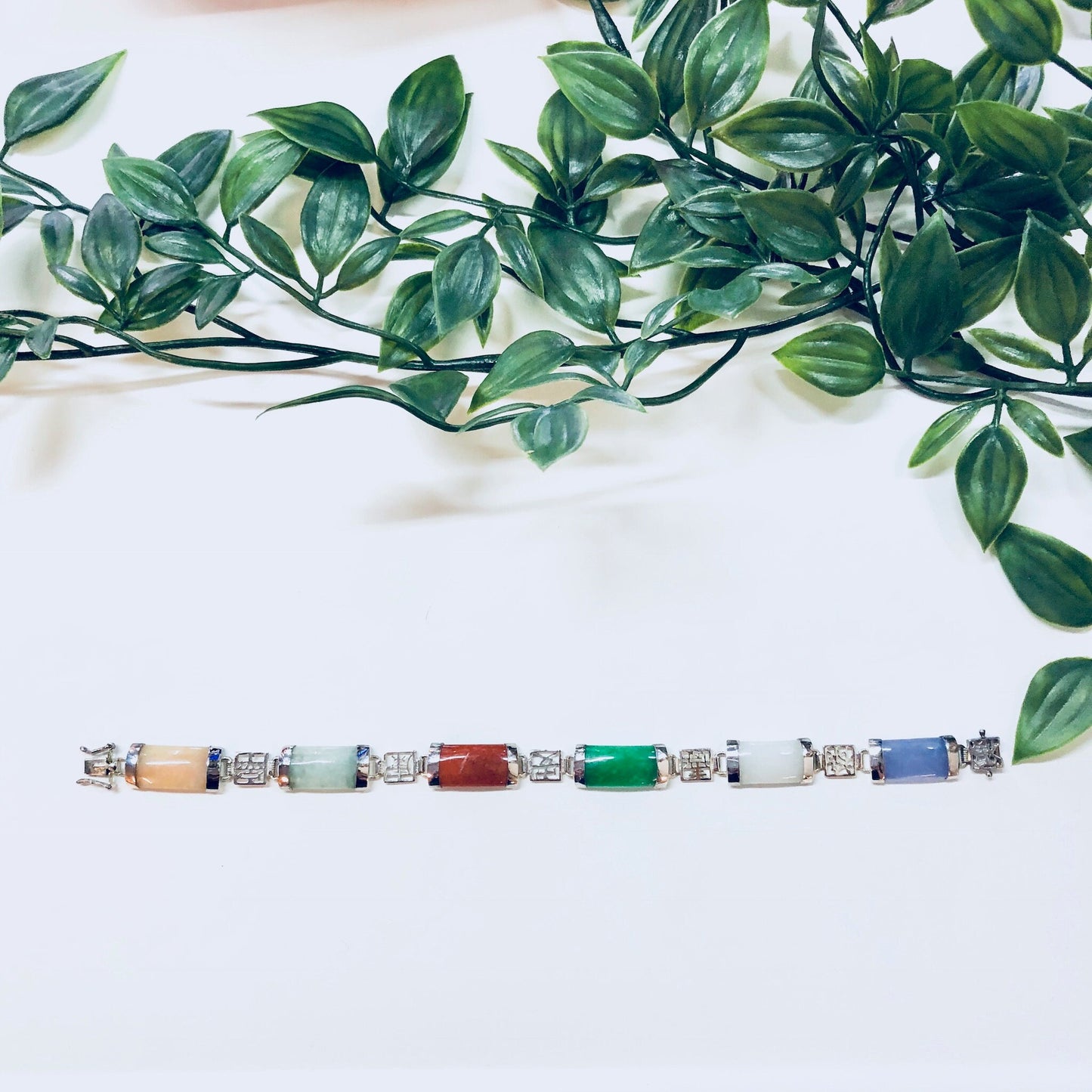 Vintage sterling silver link bracelet with natural stones in jade green, purple, orange, white and red colors, set against green foliage background