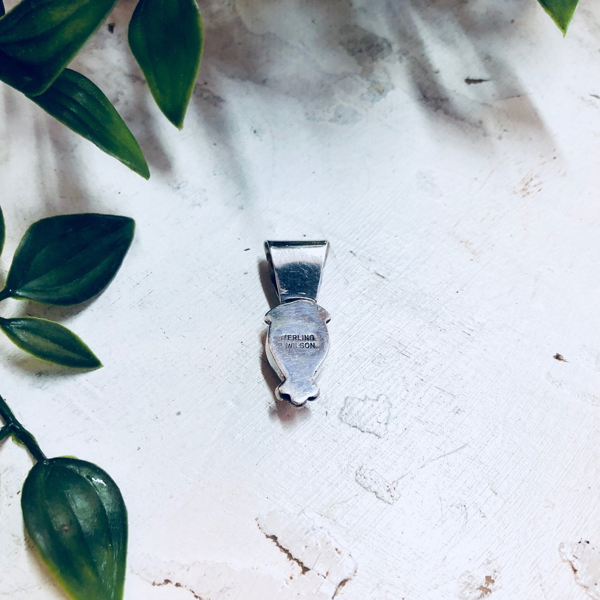 Vintage sterling silver pendant necklace with pink rhodochrosite stone lying on white textured surface next to green leaves