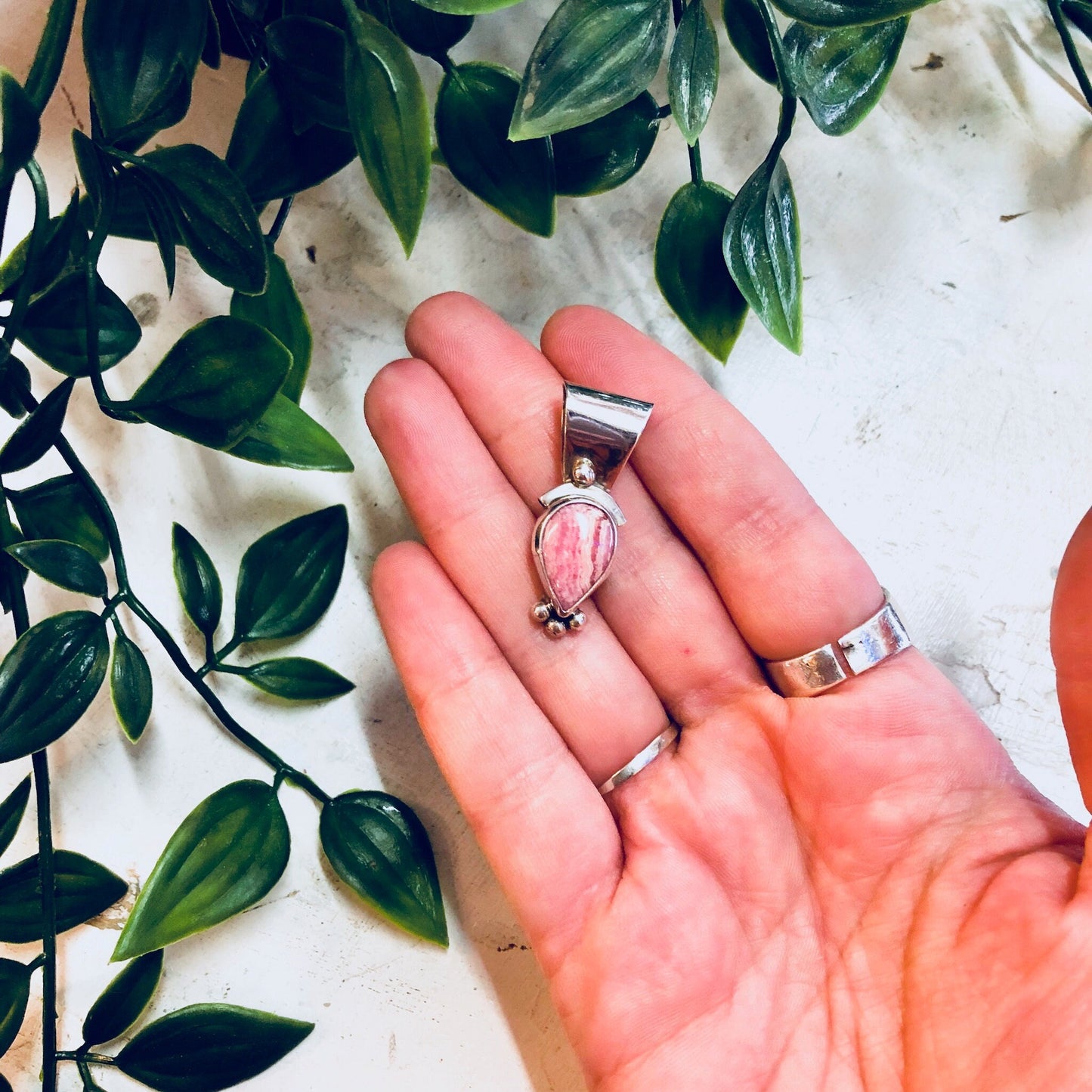 Vintage sterling silver pendant with pink rhodochrosite stone held in hand against green foliage background