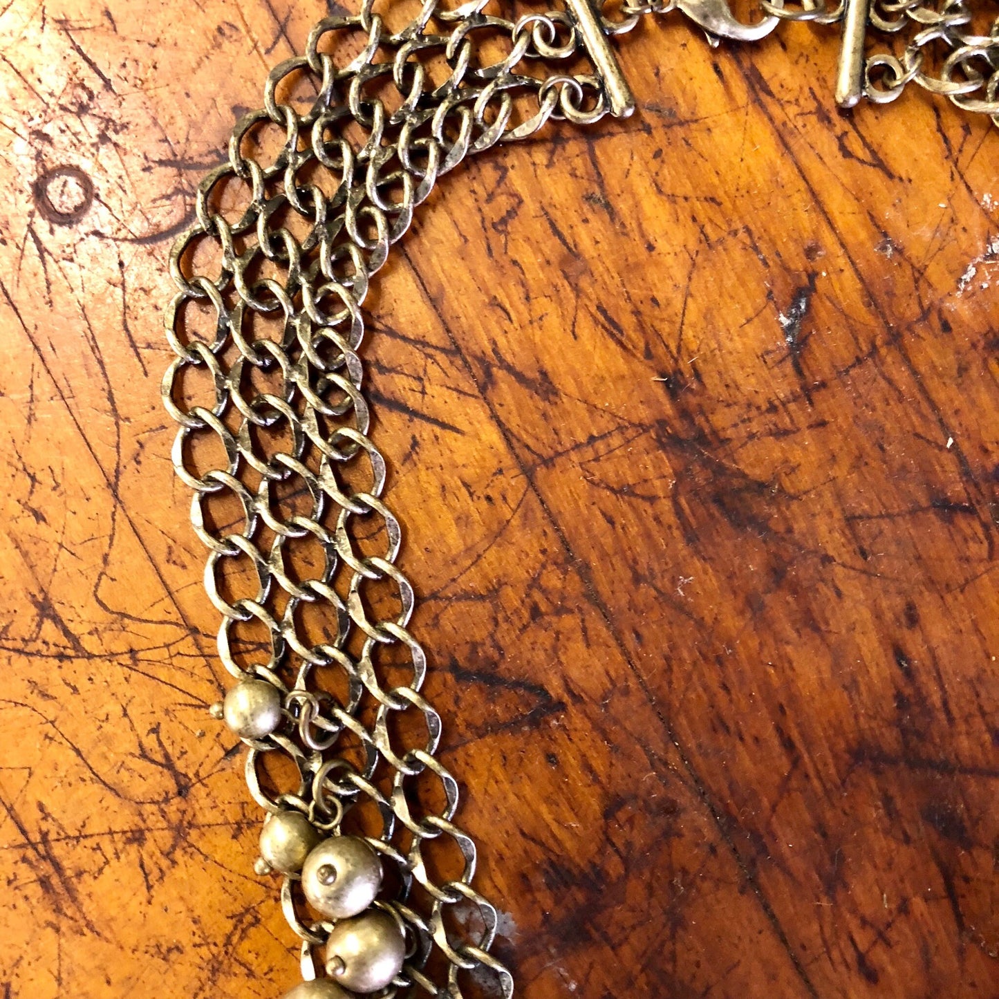 Vintage brass-toned bib necklace with interlocking chain links and dangling ball charms on a scratched wooden surface.