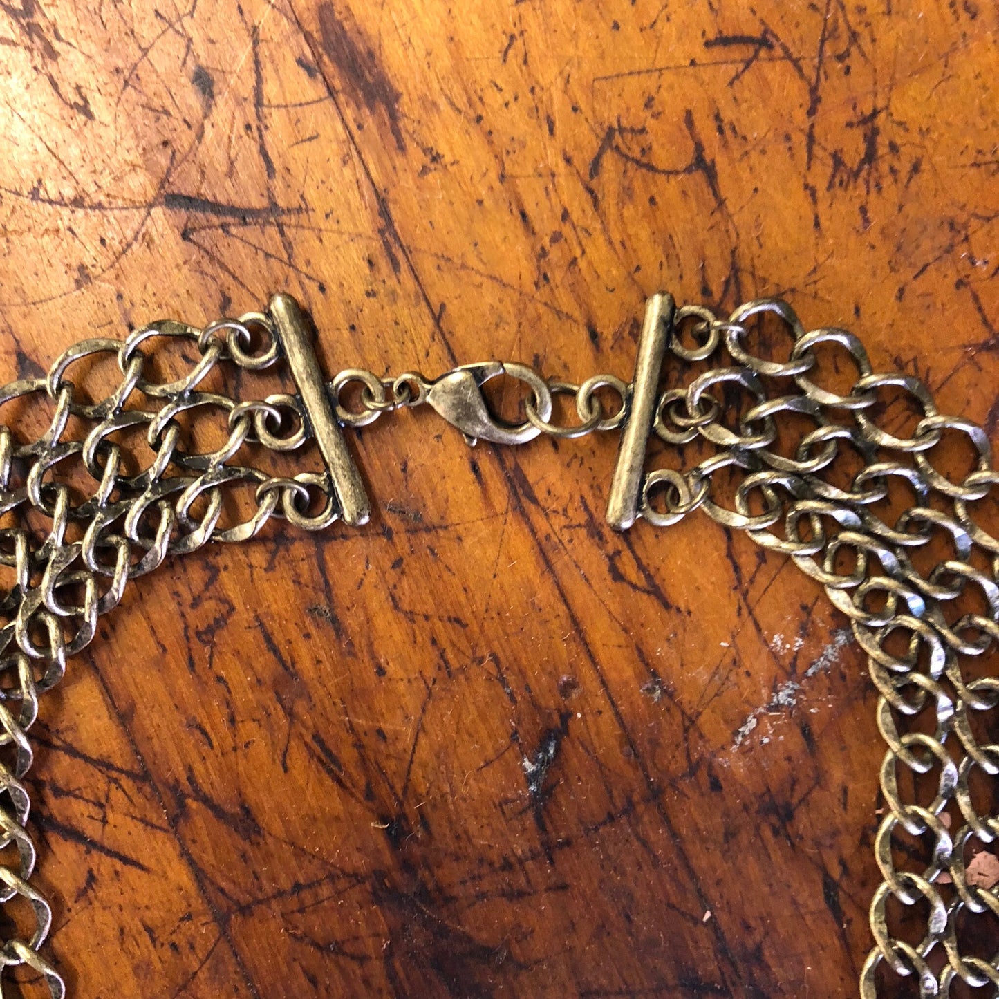 Vintage gold-toned brass choker necklace with chain link design on weathered wooden surface.