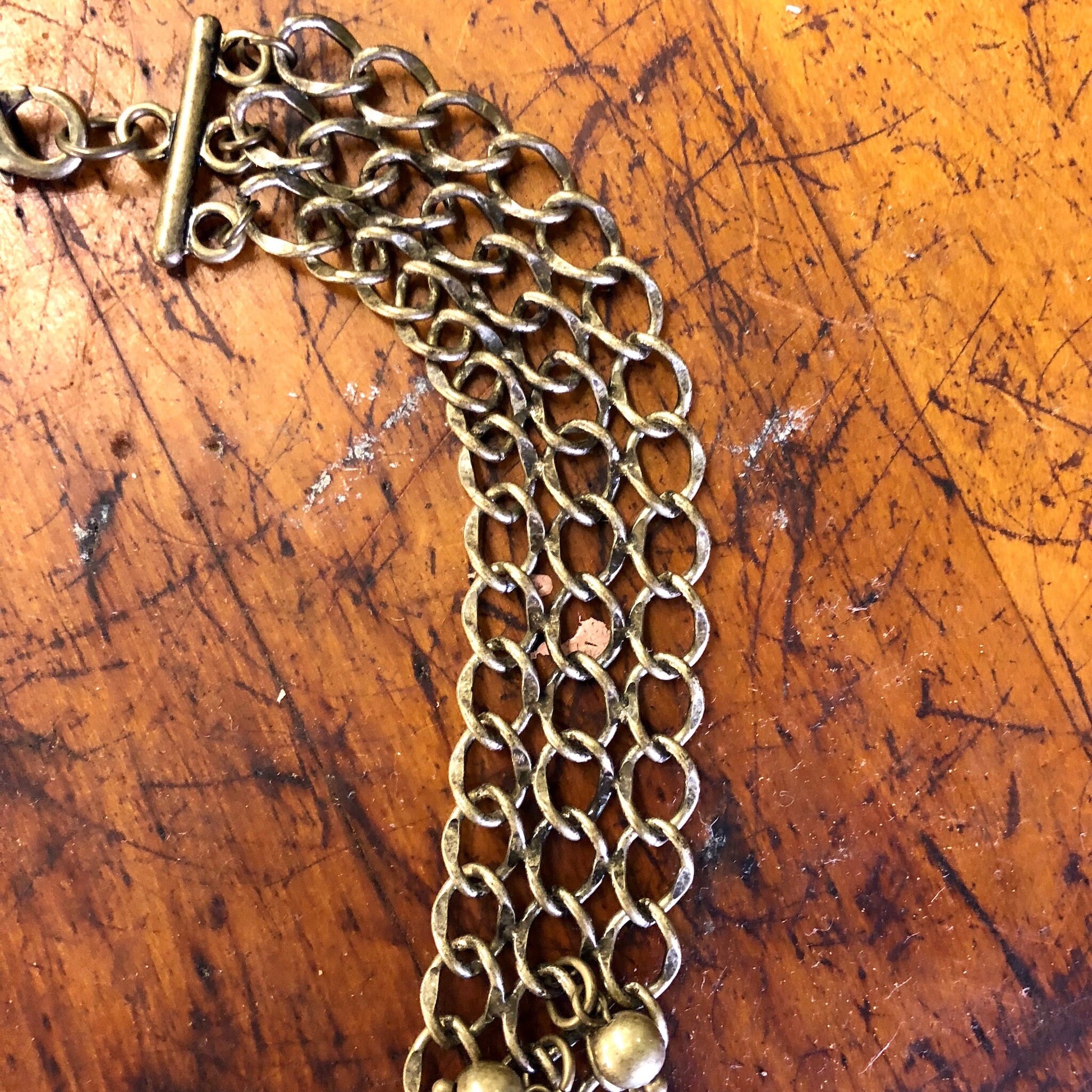 Vintage gold-toned brass bib statement necklace with multiple chain strands on scratched wooden surface