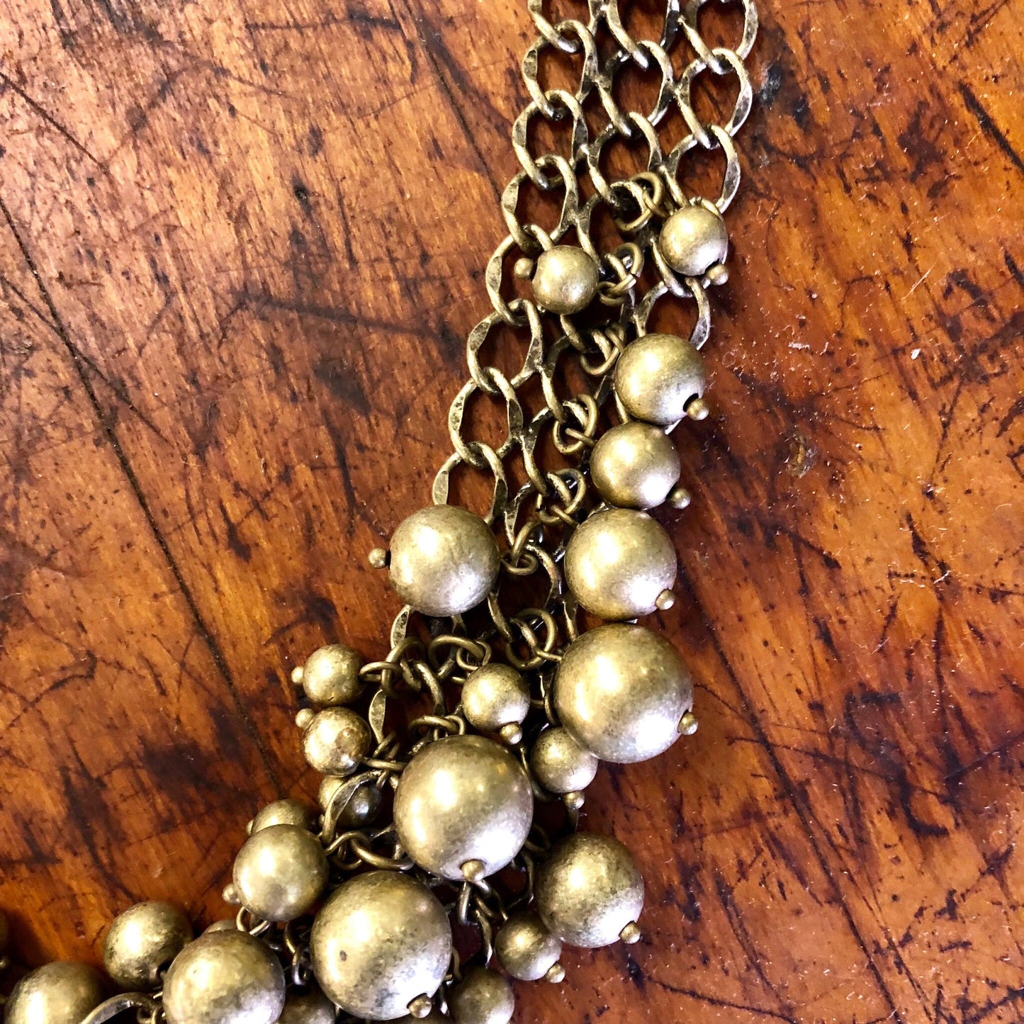 Vintage gold-toned bib necklace with multiple chains and round beads on a wooden surface.