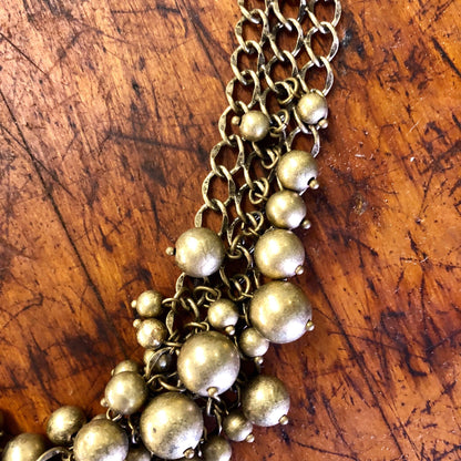 Vintage gold-toned bib necklace with multiple chains and round beads on a wooden surface.