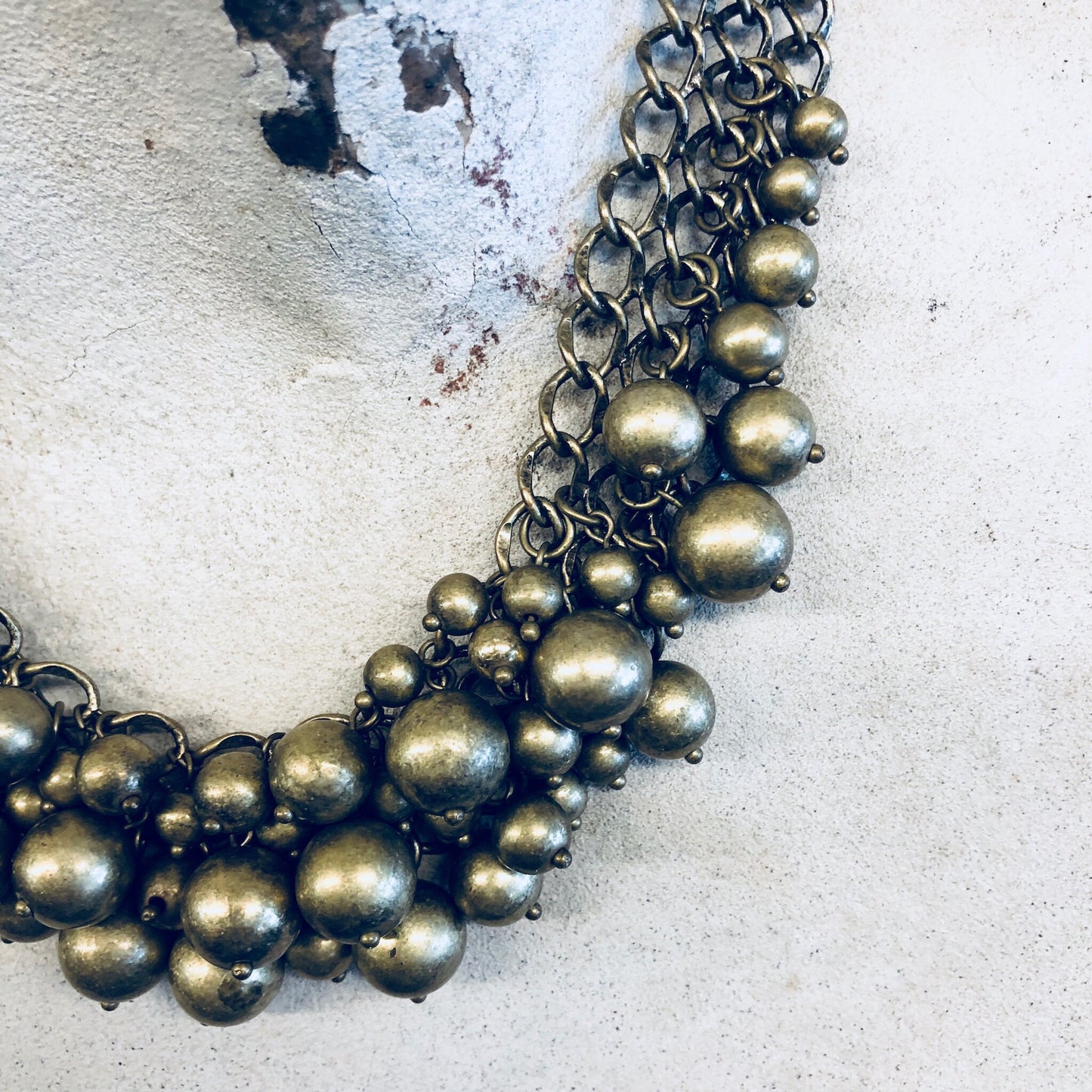 Vintage gold-toned bib necklace with multiple strands of brass ball beads, forming a statement choker-style costume jewelry piece against a textured white background.