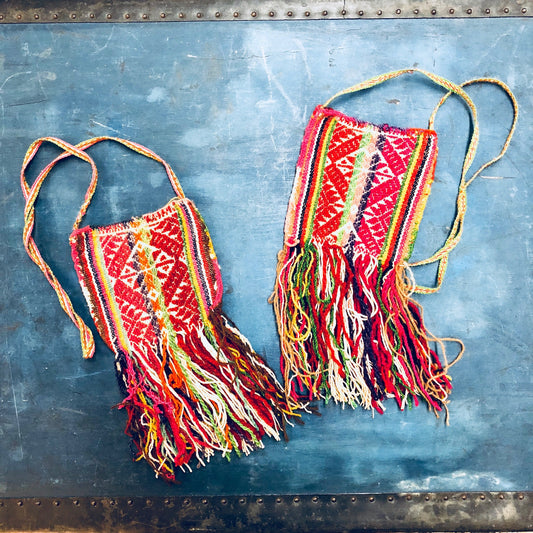 Vintage woven shoulder bag with colorful red, green, pink and yellow geometric patterns and fringe detail on textured blue background