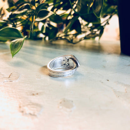 Vintage silver spoon ring with floral design, handcrafted from Rogers Bros. cutlery, displayed on rustic stone surface with greenery in background