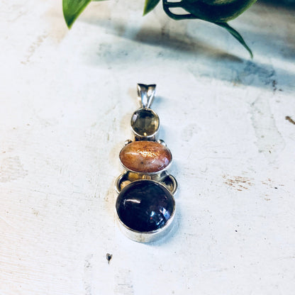 Vintage silver pendant necklace with smoky quartz, orange and purple natural stones on a light background with plant leaves.