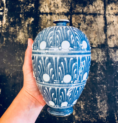 Vintage blue and white ceramic vase with polka dot pattern held in front of weathered concrete background