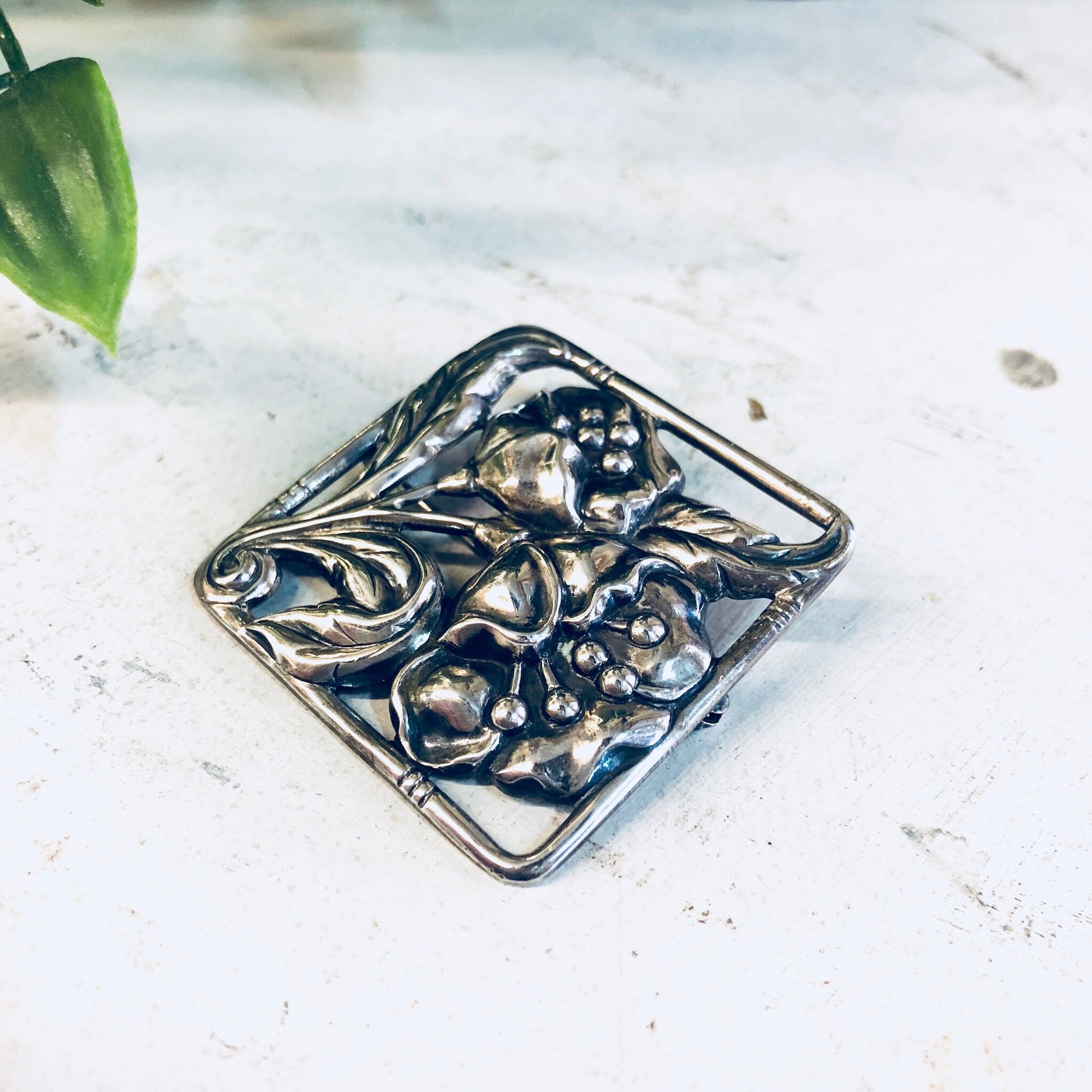 Vintage Dancraft sterling silver floral brooch pin with intricate blooming flower design from the 1940s, photographed on a white marble surface next to green leaves.