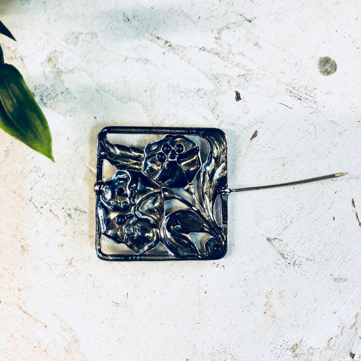 Vintage Dancraft sterling silver floral brooch pin with blooming flower design from the 1940s, photographed on a distressed white surface with leaves.