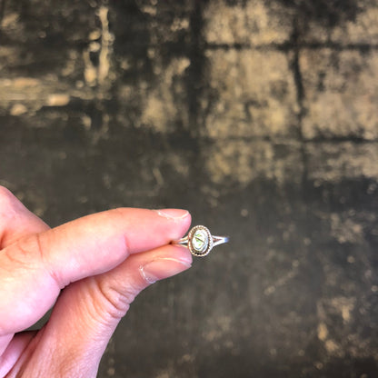 Vintage sterling silver pinky ring with abalone shell inlay, held in hand against rustic wooden background