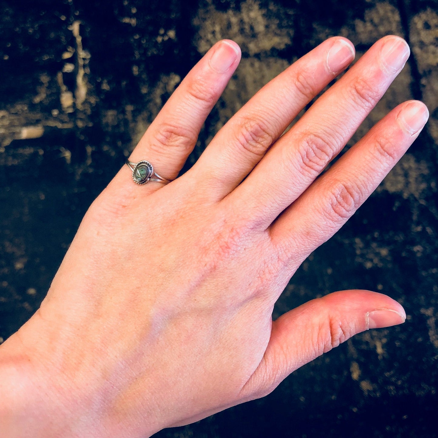 Vintage sterling silver pinky ring with small abalone shell inlay, shown on hand against dark textured background.