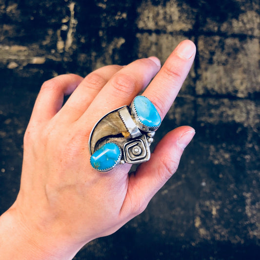 Hand wearing a vintage silver ring with turquoise inlay and horn design against a dark textured background, highlighting Southwestern style statement jewelry.