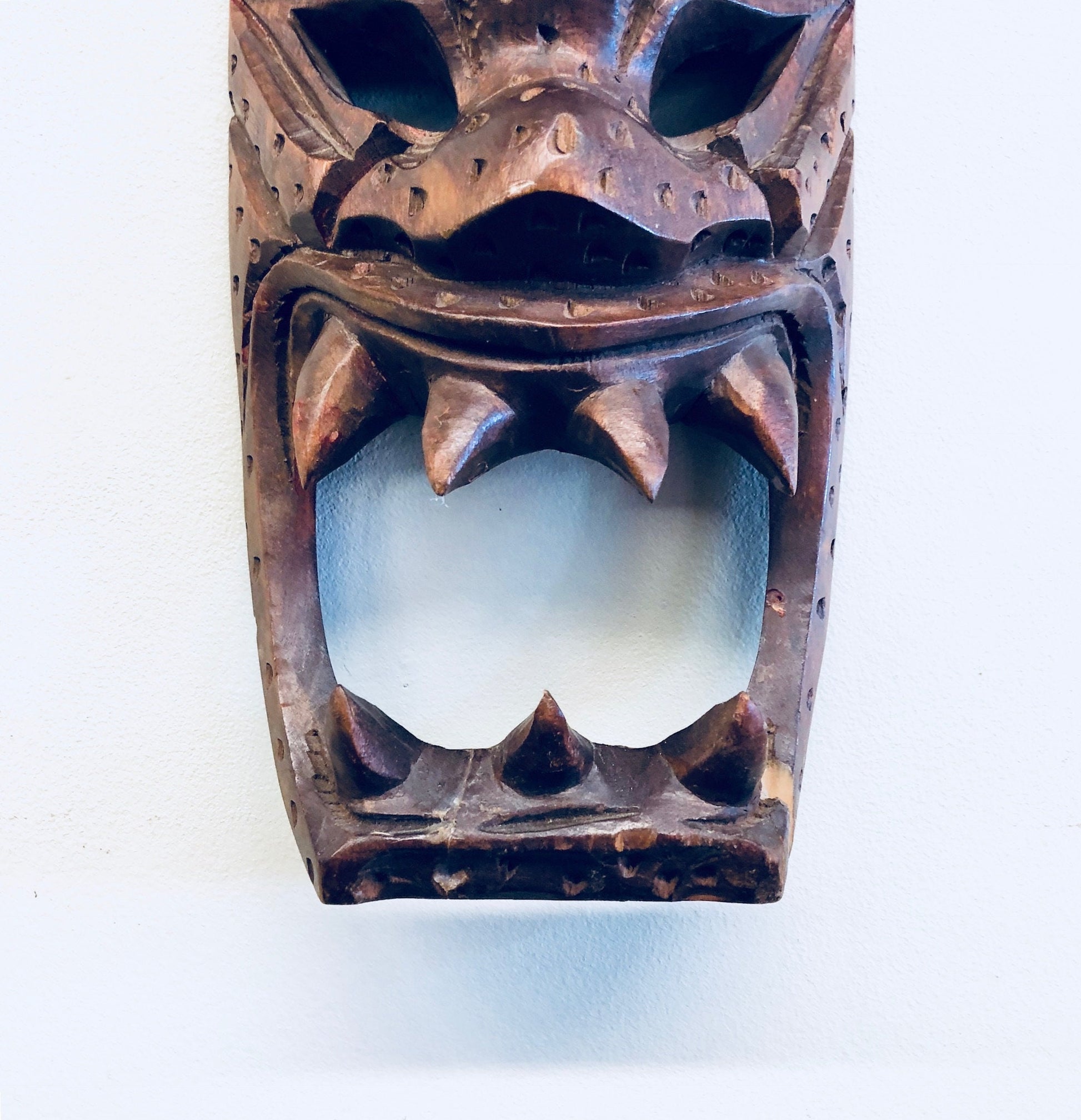Vintage hand carved wooden mask with exaggerated features and teeth, in brown tones, suitable for primitive wall decor or display.