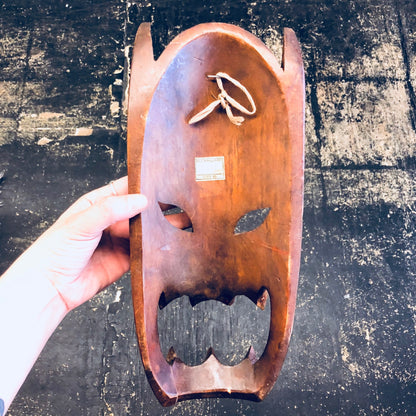 Vintage wooden carved mask with open mouth design, used for wall decor or primitive home decor, shown against a grungy backdrop.