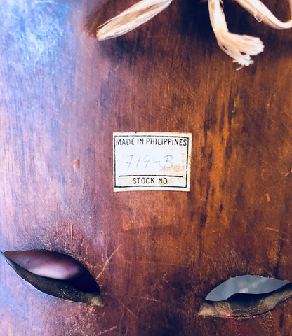 Vintage hand carved wooden mask with "Made in Philippines" label, surrounded by weathered brown wood. Primitive wall decor.