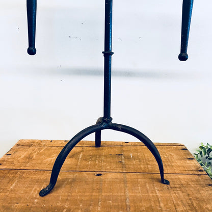 Vintage wrought iron tripod candle holder on rustic wooden table against white wall background, suitable for rustic home decor, mantle piece, or centerpiece.