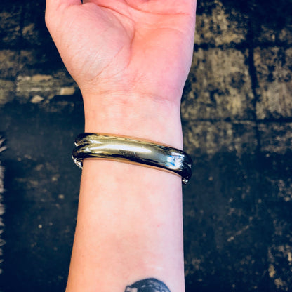 Vintage gold-toned hinged snake bracelet with rhinestones worn on a wrist against a grungy brick wall background.