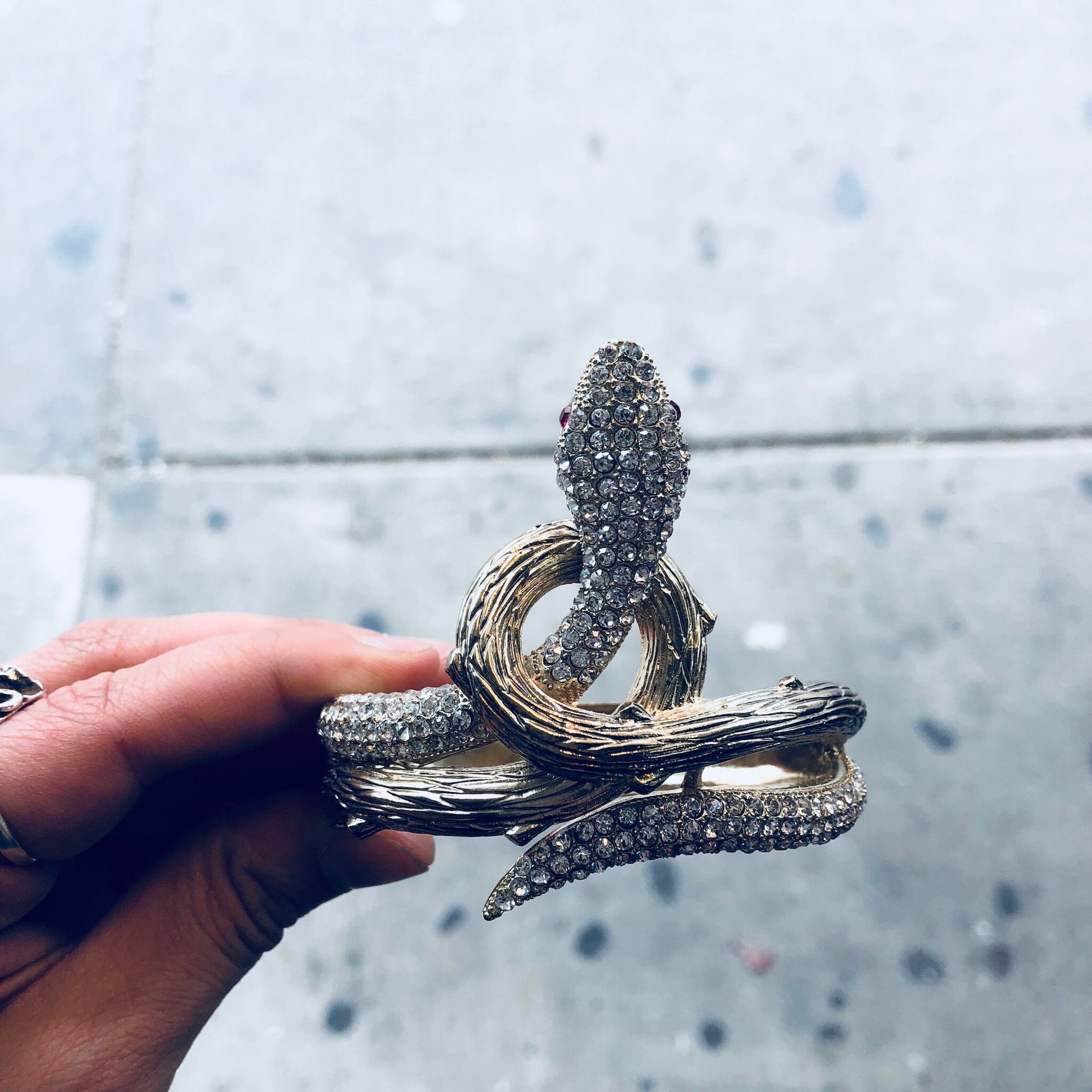 Vintage gold-toned hinged snake bracelet with rhinestones, held in hand against gray background