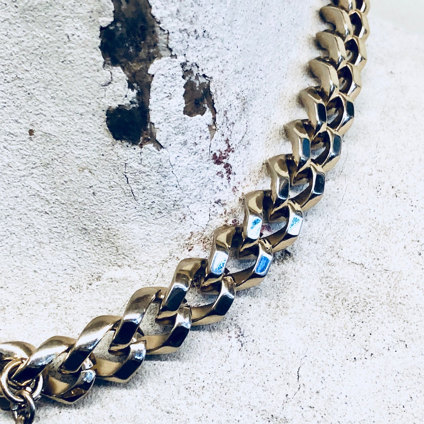 Vintage gold-toned Monet necklace with thick chain links and blue stone pendant against weathered concrete background