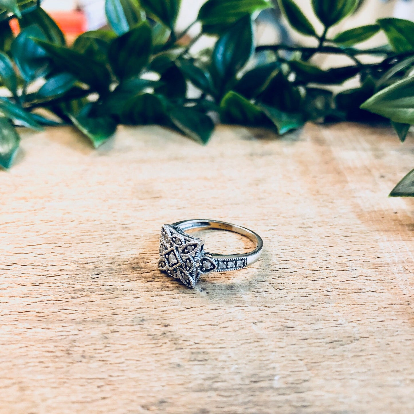 Vintage 14K white gold Art Deco diamond engagement ring on wooden surface with greenery in background