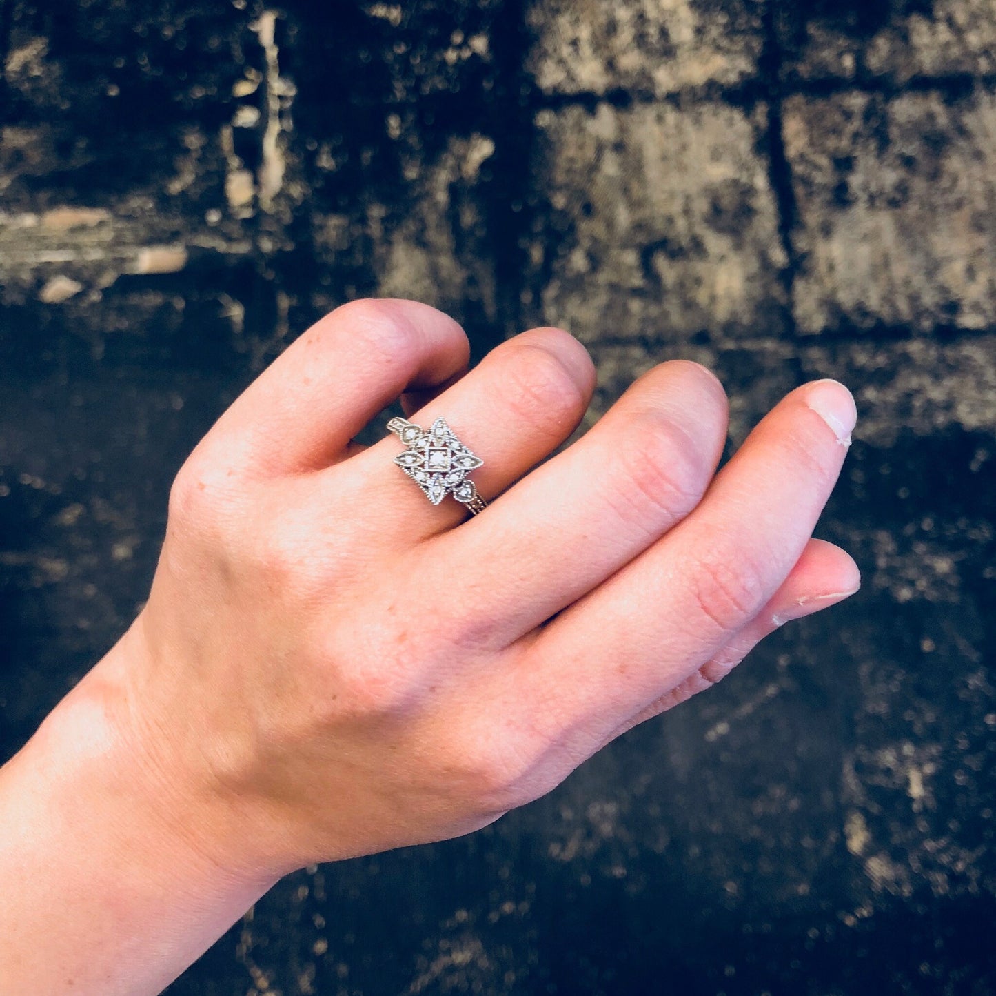 Vintage 14K white gold Art Deco diamond engagement ring on hand against weathered wooden background