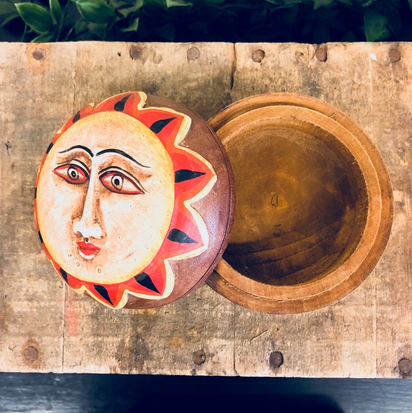 Vintage hand-carved wooden jewelry box with a colorful sun face design in red, orange and yellow tones on the lid, displayed on a rustic wooden surface.