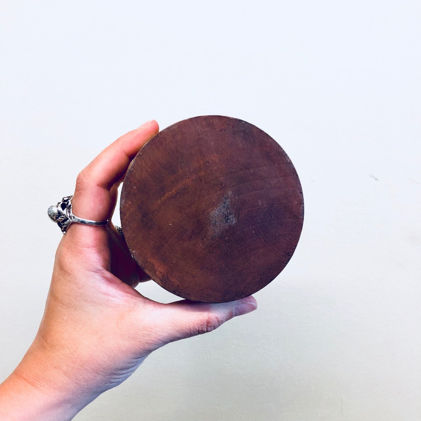 Hand holding a round, wooden carved box with a sun face design on the lid against a plain white background.