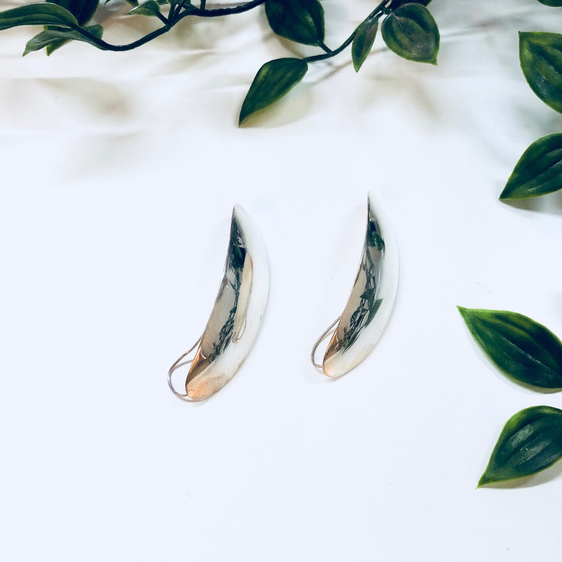 Vintage sterling silver statement earrings with minimal curved design surrounded by green leaves, unique anniversary gift jewelry