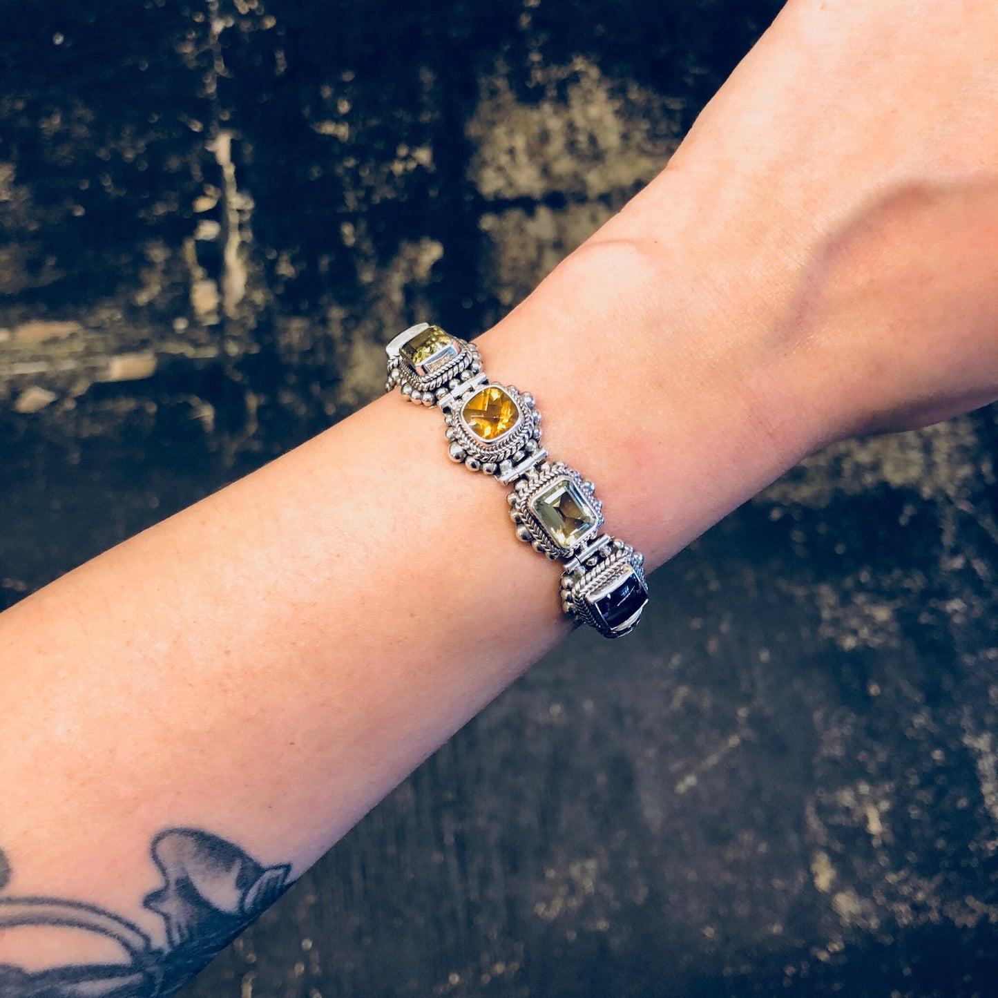 Vintage sterling silver gemstone link bracelet with amethyst, peridot and citrine stones, shown on a wrist against a dark textured background.