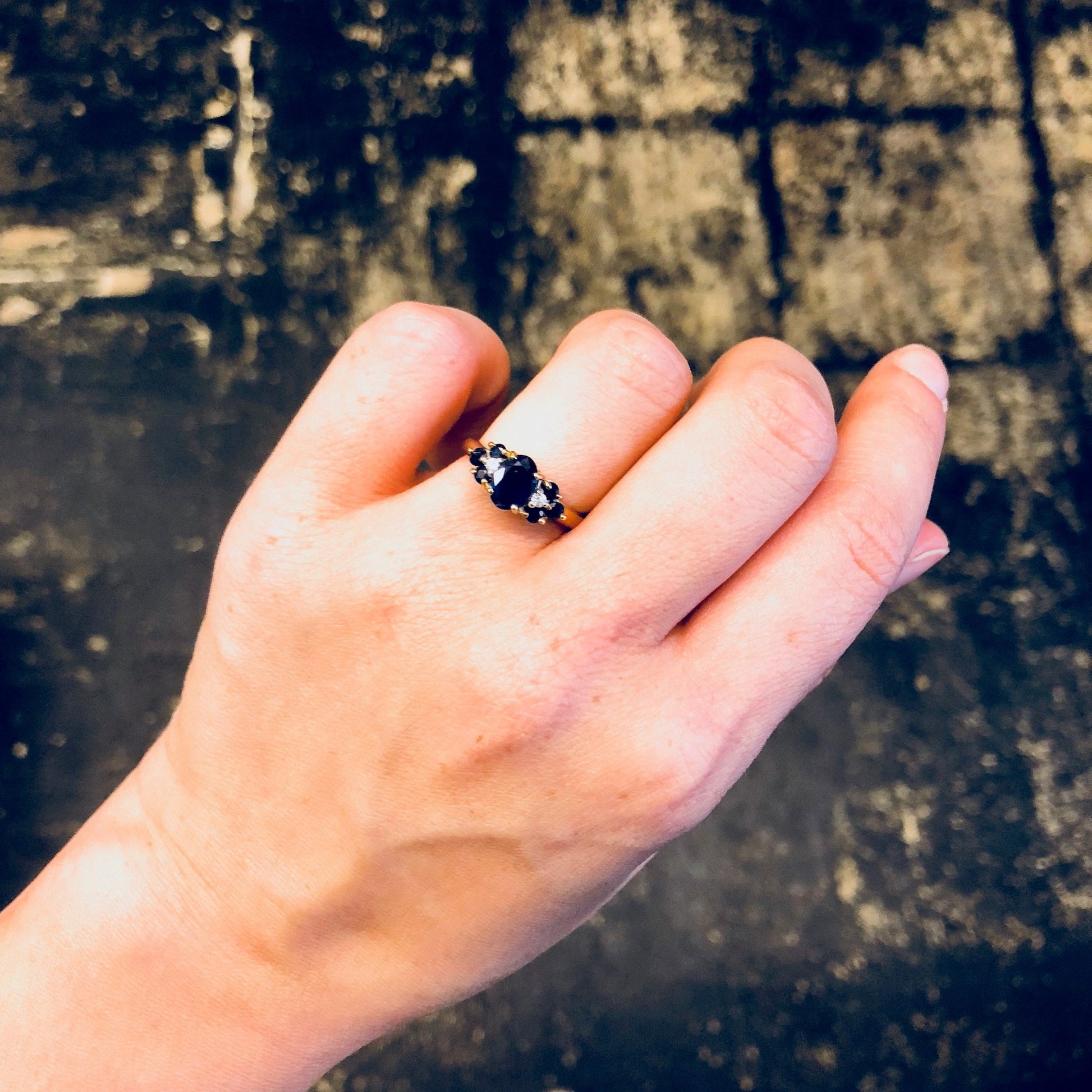Vintage sapphire and 14K yellow gold ring displayed on a hand against a distressed wooden background.