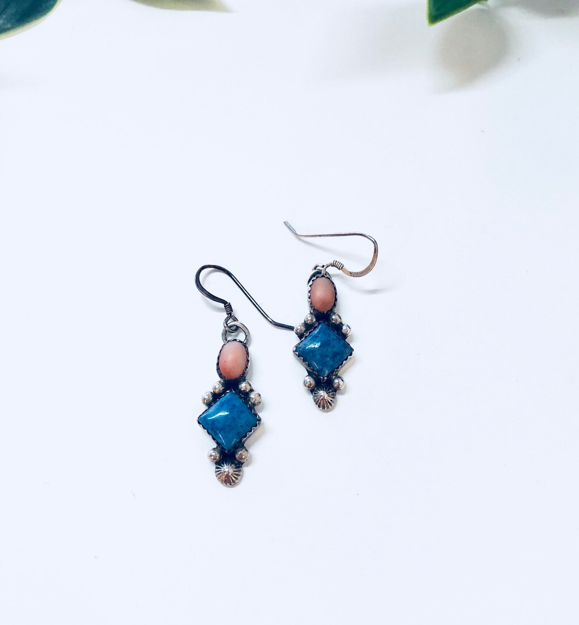 Vintage silver and blue gemstone dangle earrings on white background with green leaves